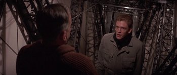 Movie still from “The Hindenburg” (1975), directed by Robert Wise – A man standing next to another man in front of a bridge; Medium shot, Over the shoulder angle