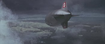 Movie still from “The Hindenburg” (1975), directed by Robert Wise – An airship flying in the sky over a body of water; Extreme Wide shot, High angle