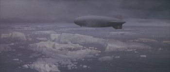 Movie still from “The Hindenburg” (1975), directed by Robert Wise – An airliner is flying over the ocean on a cloudy day; Extreme Wide shot, Overhead angle