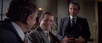 Movie still from “The Hindenburg” (1975), directed by Robert Wise – A man in a suit and tie next to two other men; Medium shot, Over the shoulder angle