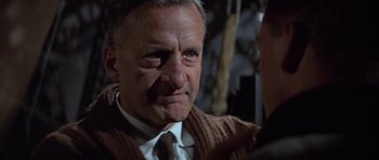 Movie still from “The Hindenburg” (1975), directed by Robert Wise – An older man wearing a sweater and a tie; Close Up shot, Over the shoulder angle