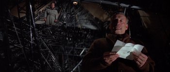 Movie still from “The Hindenburg” (1975), directed by Robert Wise – A man holding a paper in front of an image of a woman; Medium shot, Low angle