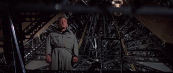 Movie still from “The Hindenburg” (1975), directed by Robert Wise – A man standing in front of a bunch of metal structures; Medium shot, Low angle
