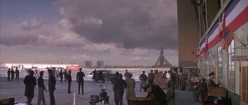 Movie still from “The Hindenburg” (1975), directed by Robert Wise – A group of people standing on a dock near a body of water; Extreme Wide shot, High angle