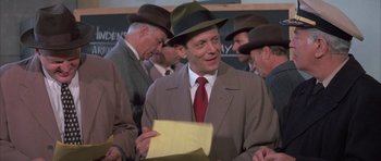 Movie still from “The Hindenburg” (1975), directed by Robert Wise – A man wearing a suit and a hat holding a piece of paper; Medium shot, Over the shoulder angle