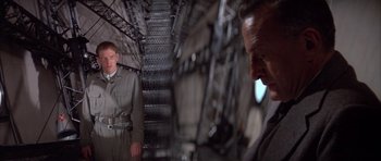 Movie still from “The Hindenburg” (1975), directed by Robert Wise – A man in a suit standing next to another man in a suit; Medium shot, Low angle