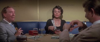 Movie still from “The Hindenburg” (1975), directed by Robert Wise – A woman sitting at a table holding a pair of scissors in her hand; Medium shot, Over the shoulder angle