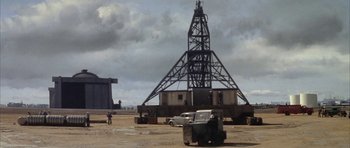 Movie still from “The Hindenburg” (1975), directed by Robert Wise – An oil rig sits in the middle of a field; Extreme Wide shot, High angle