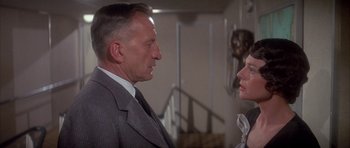 Movie still from “The Hindenburg” (1975), directed by Robert Wise – An older man in a suit and tie talking to an older woman; Close Up shot, Over the shoulder angle
