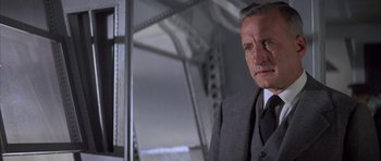 Movie still from “The Hindenburg” (1975), directed by Robert Wise – A man in a suit and tie standing in front of a bridge; Close Up shot, Low angle