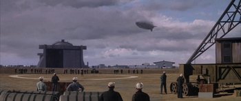 Movie still from “The Hindenburg” (1975), directed by Robert Wise – A group of people standing on top of a dirt field; Extreme Wide shot, Low angle