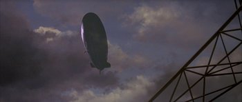 Movie still from “The Hindenburg” (1975), directed by Robert Wise – An airship is flying in the sky on a cloudy day; Extreme Wide shot, Low angle