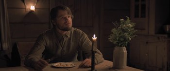 Movie still from “The Homesman” (2014), directed by Tommy Lee Jones – A man sitting at a dinner table with a lit candle; Medium shot, Over the shoulder angle
