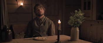 Movie still from “The Homesman” (2014), directed by Tommy Lee Jones – A man sitting at a dinner table with a candle in the background; Medium shot, Over the shoulder angle