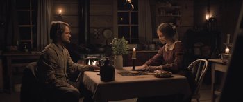 Movie still from “The Homesman” (2014), directed by Tommy Lee Jones – Two people sitting at a table with a lit candle; Medium shot, Over the shoulder angle