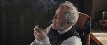Movie still from “The Homesman” (2014), directed by Tommy Lee Jones – An older man smoking a cigarette while wearing a vest and tie; Close Up shot, Over the shoulder angle