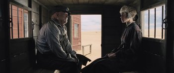 Movie still from “The Homesman” (2014), directed by Tommy Lee Jones – A man and a woman sitting on a bench in front of an open door; Medium shot, Over the shoulder angle