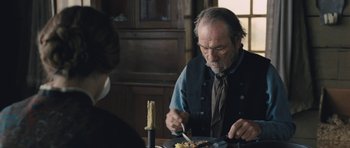 Movie still from “The Homesman” (2014), directed by Tommy Lee Jones – An older man sitting at a dinner table with a knife and fork in his hand; Close Up shot, Over the shoulder angle