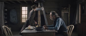 Movie still from “The Homesman” (2014), directed by Tommy Lee Jones – An old man sitting at a table with a bowl of food in front of a woman; Wide shot, Over the shoulder angle
