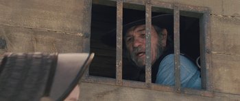 Movie still from “The Homesman” (2014), directed by Tommy Lee Jones – An old man with a beard wearing a cowboy hat looking out of a jail cell; Close Up shot, Over the shoulder angle