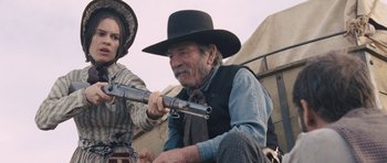 Movie still from “The Homesman” (2014), directed by Tommy Lee Jones – An old man sitting next to a young woman holding a rifle; Medium shot, Low angle
