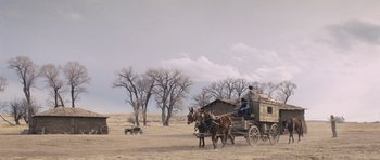 Movie still from “The Homesman” (2014), directed by Tommy Lee Jones – A man riding on the back of a horse drawn carriage; Extreme Wide shot, Low angle