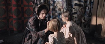 Movie still from “The Homesman” (2014), directed by Tommy Lee Jones – A woman is putting a face mask on two young girls; Medium shot, Over the shoulder angle