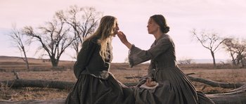 Movie still from “The Homesman” (2014), directed by Tommy Lee Jones – Two women sitting on the ground and one of them is eating a piece of cake; Medium shot, Over the shoulder angle
