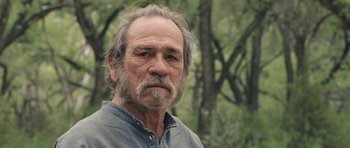 Movie still from “The Homesman” (2014), directed by Tommy Lee Jones – An older man with a beard and a gray shirt; Close Up shot, Over the shoulder angle