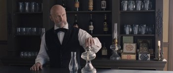 Movie still from “The Homesman” (2014), directed by Tommy Lee Jones – A man in a black vest and a white bow tie is standing at a bar; Medium shot, Low angle