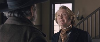 Movie still from “The Homesman” (2014), directed by Tommy Lee Jones – A man in a suit and a hat standing next to another man in front of a window; Close Up shot, Over the shoulder angle