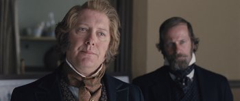 Movie still from “The Homesman” (2014), directed by Tommy Lee Jones – A man in a suit and tie standing next to another man in a suit and tie; Close Up shot, Over the shoulder angle