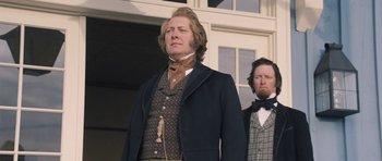 Movie still from “The Homesman” (2014), directed by Tommy Lee Jones – A man standing next to another man wearing a suit; Medium shot, Low angle