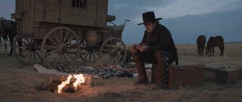 Movie still from “The Homesman” (2014), directed by Tommy Lee Jones – A man sitting on the ground next to an open fire; Wide shot, Over the shoulder angle
