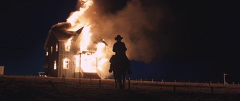 Movie still from “The Homesman” (2014), directed by Tommy Lee Jones – A man riding a horse in front of a burning building at night; Wide shot, Low angle