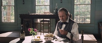 Movie still from “The Homesman” (2014), directed by Tommy Lee Jones – An older man sitting at a table with a plate of food in front of him; Medium shot, Over the shoulder angle
