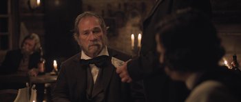 Movie still from “The Homesman” (2014), directed by Tommy Lee Jones – An older man in a suit and tie holding a money bill; Medium shot, Over the shoulder angle