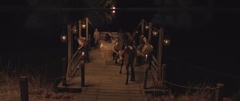 Movie still from “The Homesman” (2014), directed by Tommy Lee Jones – A group of people sitting and standing on a dock at night; Extreme Wide shot, High angle