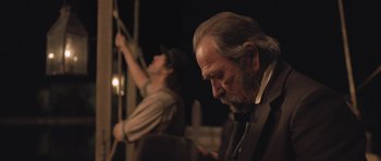 Movie still from “The Homesman” (2014), directed by Tommy Lee Jones – A man in a suit and tie looking down at something; Medium shot, Over the shoulder angle