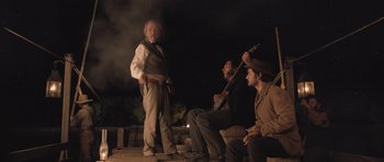 Movie still from “The Homesman” (2014), directed by Tommy Lee Jones – A group of men sitting on top of a wooden floor; Medium shot, Low angle