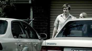 Movie still from “The Horseman” (2008), directed by Steven Kastrissios – A man standing in front of two parked cars; Medium shot, Over the shoulder angle