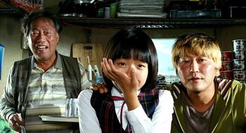Movie still from “The Host” (2006), directed by Bong Joon Ho – A young girl covers her mouth with her hand while standing next to an older man and woman; Close Up shot, Low angle