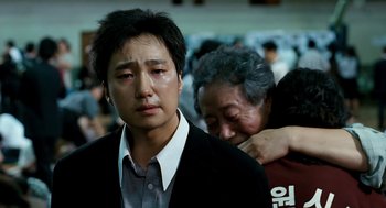 Movie still from “The Host” (2006), directed by Bong Joon Ho – An asian man and an older woman hug in front of a crowd; Close Up shot, Over the shoulder angle