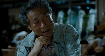 Movie still from “The Host” (2006), directed by Bong Joon Ho – An older man is sitting with his chin resting on his hand; Close Up shot, Over the shoulder angle