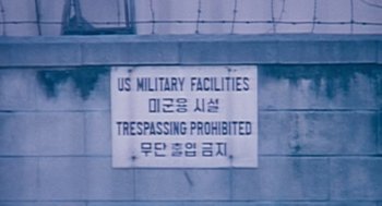 Movie still from “The Host” (2006), directed by Bong Joon Ho – A sign on the side of a building that says " us military facilities " and " trespassing prohibited "; Extreme Close Up shot, Low angle