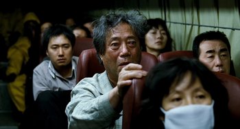 Movie still from “The Host” (2006), directed by Bong Joon Ho – An older man sitting on a train with other passengers; Close Up shot, Over the shoulder angle