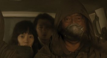 Movie still from “The Host” (2006), directed by Bong Joon Ho – A man wearing a gas mask while standing next to two other people; Close Up shot, Low angle