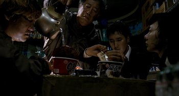Movie still from “The Host” (2006), directed by Bong Joon Ho – Two people sitting at a table with a bowl of food; Medium shot, High angle