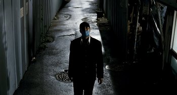 Movie still from “The Host” (2006), directed by Bong Joon Ho – A man in a suit with a mask on his face walking down a street; Wide shot, High angle