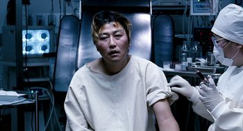 Movie still from “The Host” (2006), directed by Bong Joon Ho – A man sitting in front of a chair with gloves on; Close Up shot, High angle